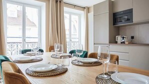 Comedor con una mesa de madera dispuesta para seis personas, sillas alrededor y una cocina con electrodomésticos modernos.