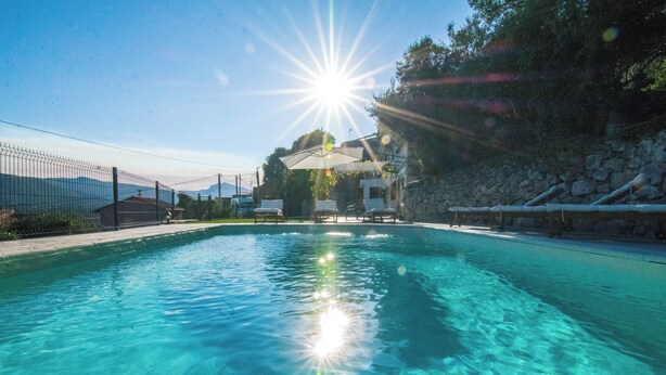 Una piscina cristalina con el sol brillando directamente arriba, rodeada por un muro de piedra y una zona vallada.