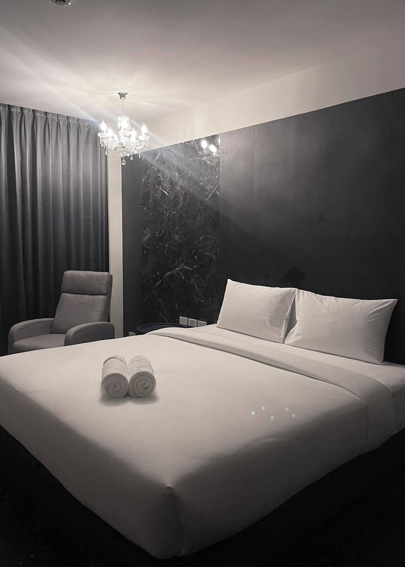 Una habitación de hotel moderna con una cama grande, una silla, un muro decorativo de mármol y un candelabro.