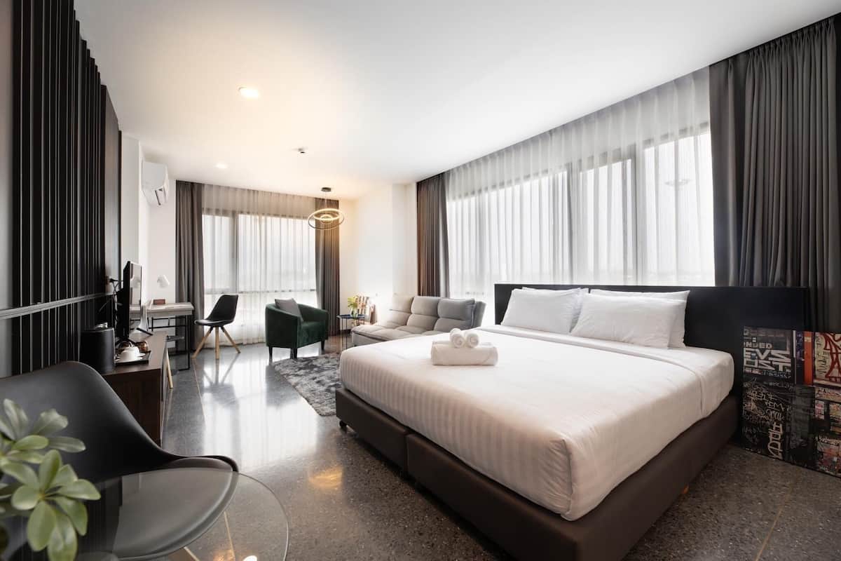 A modern hotel room with a large bed, a desk, a chair, and a sofa.