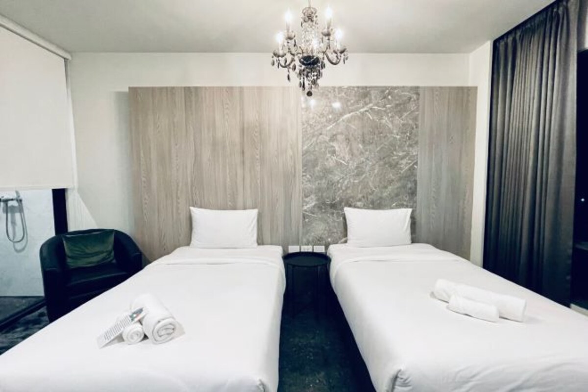 Habitación de hotel con dos camas, una araña, un panel de madera decorativo y vistas a un edificio.