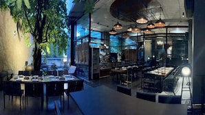 Un restaurante con una decoración moderna, que cuenta con una larga mesa de comedor, varios espacios de estar e iluminación colgante.