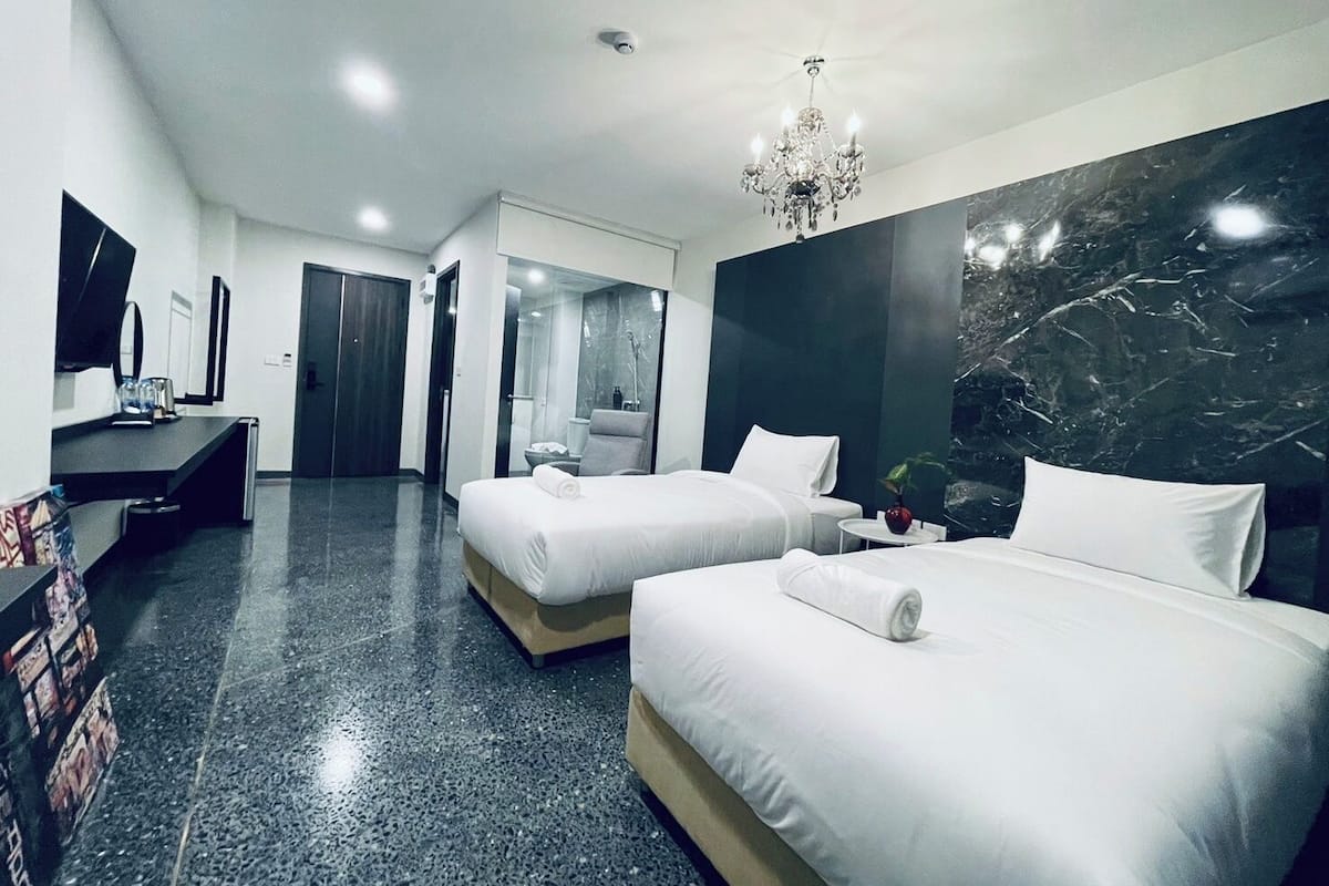 A modern hotel room with two beds, a large mirror, a TV, and a marble accent wall.