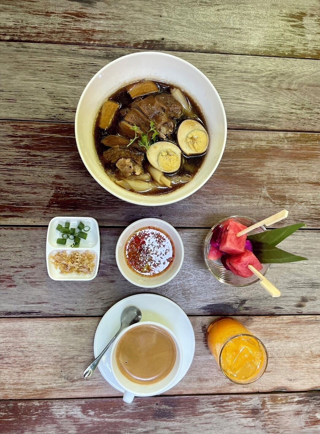 A meal with a bowl of soup, a small dish of pickled vegetables, a cup of coffee, a glass of juice, and a dessert with fruit skewers.
