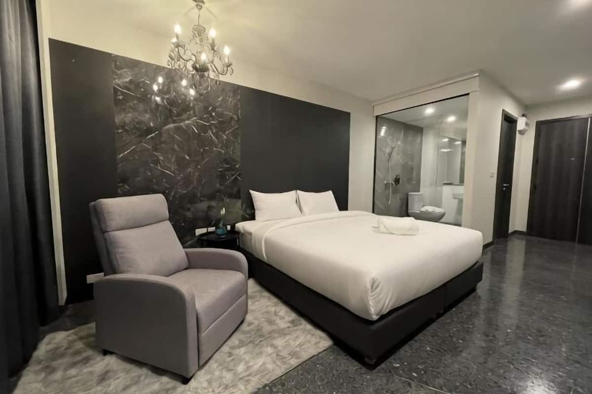 A modern bedroom with a bed, a chair, a chandelier, and a large mirror.