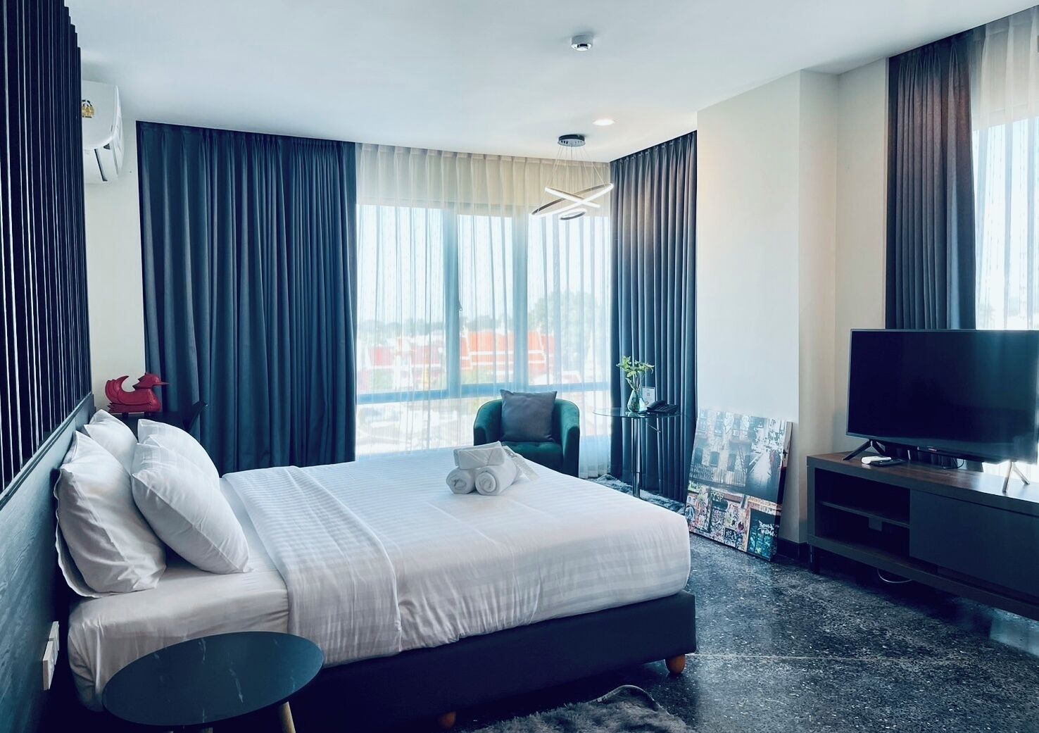 A modern hotel room with a large bed, a flat-screen TV, and a view of the city through large windows.