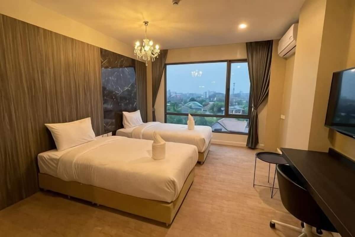A hotel room with two beds, a desk, a TV, and a large window with a city view.