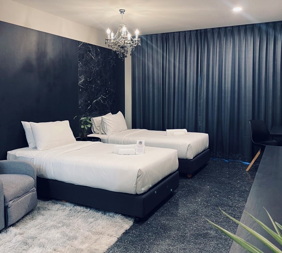 A modern hotel room with two beds, a chandelier, dark curtains, and a small desk.