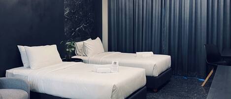 Une chambre d’hôtel moderne avec deux lits, un lustre, des rideaux foncés et un petit bureau.