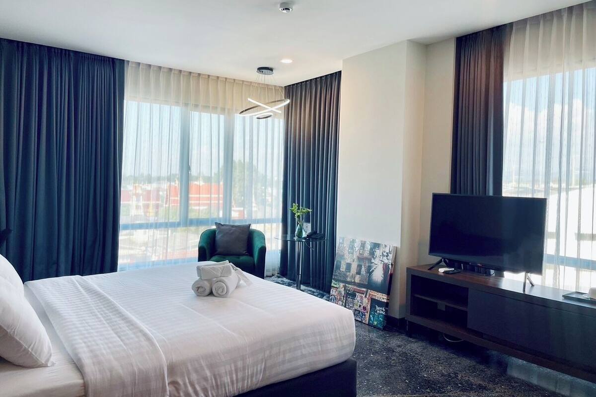 A hotel room with a large bed, a TV, a chair, and a window with curtains.