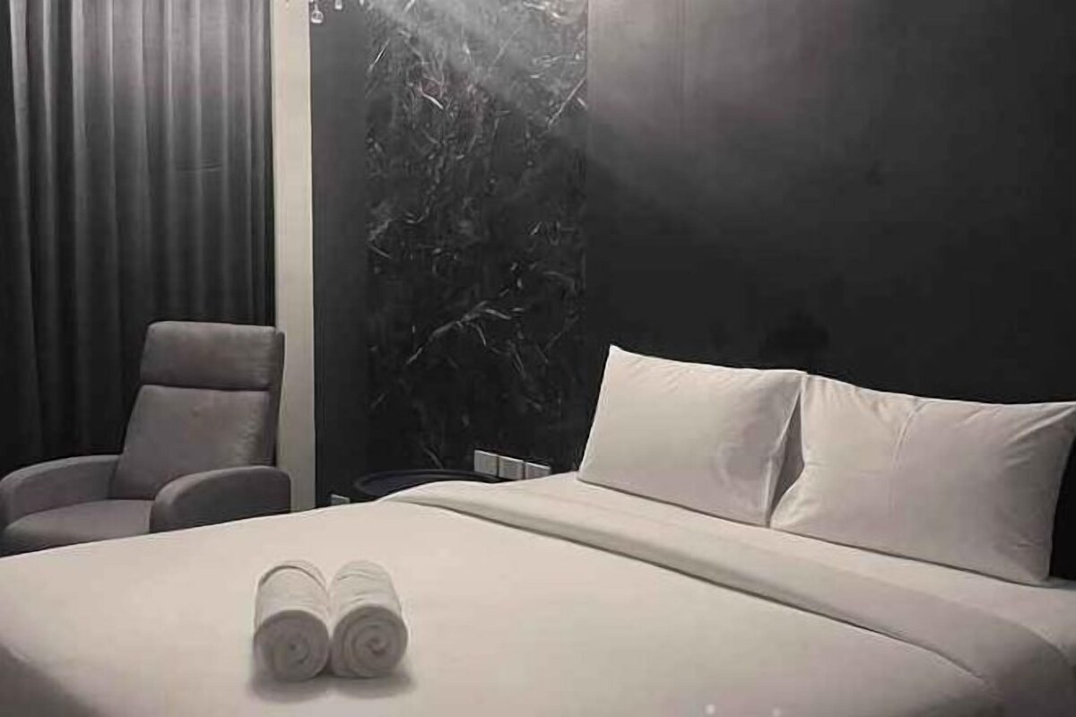 Habitación de hotel con cama, una silla y un ventanal grande.
