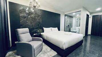 A modern hotel room with a large bed, a grey armchair, a chandelier, and a marble wall.