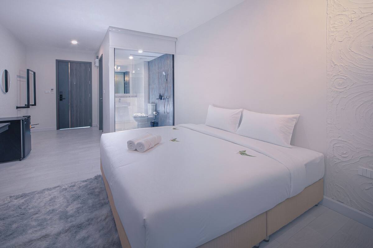 A modern hotel room with a large bed, a desk, and a bathroom visible through a glass door.