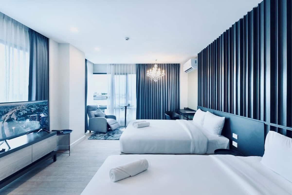 A modern hotel room with a large bed, a desk, a chair, and a TV displaying a cityscape.