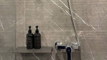 A bathroom with a shower, a handheld showerhead, a handheld shower attachment, and two bottles of shampoo on a shelf.