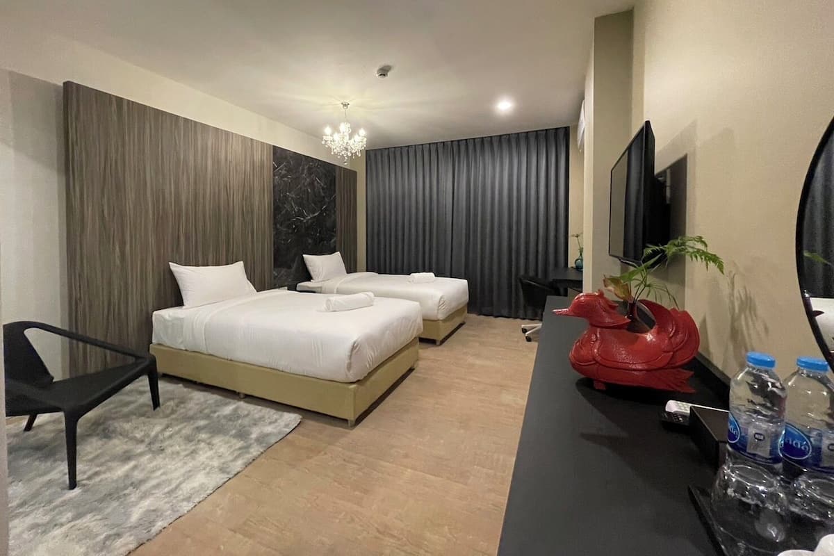 A hotel room with two beds, a desk, a chair, a TV, and a red sculpture.
