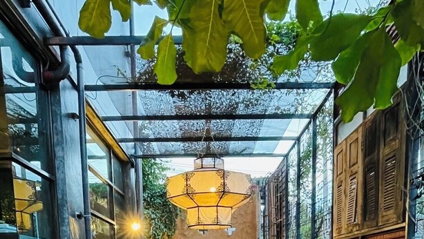 Un espacio al aire libre moderno con piscina, mesas y sillas de madera, y un farol colgante.