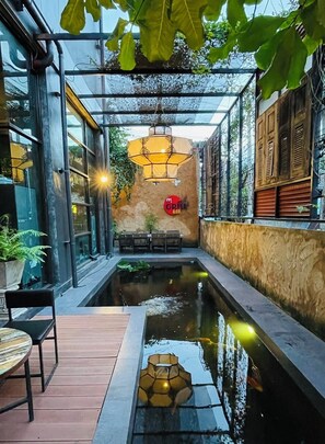 A modern outdoor seating area with a pool, wooden tables, chairs, and a hanging lantern. - SibtisHotel (Lampang)
