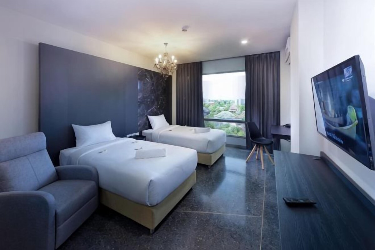 A hotel room with two beds, a sofa, a TV, and a large window.