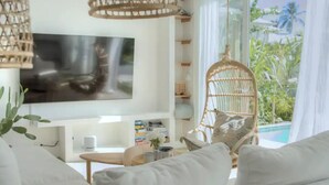 Una sala de estar moderna con un televisor de pantalla plana, sillas de mimbre y vistas a una piscina y zonas verdes.