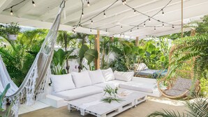 Un espacio al aire libre cubierto con un sofá blanco, una hamaca y una silla de mimbre.