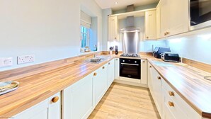 A modern kitchen with white cabinets, wooden countertops, a stainless steel range hood, and a built-in oven. - Stunning Coastal Cottage - Sleeping 6 in 2 Bedrooms - Pool and Beach Access Included. (Lovely Central Location - Detached)