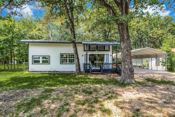 Une maison de plain-pied avec un porche, entourée d’arbres et dotée d’un garage fermé.