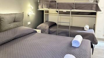 A hotel room with a large bed, a bunk bed, and a wall-mounted light fixture.