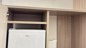 Een compacte kamer met een ingebouwde witte koelkast, een kleine prullenbak en een houten kast.