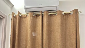 Een badkamer met een bruin douchegordijn, een witte muur en een airconditioning boven het gordijn.