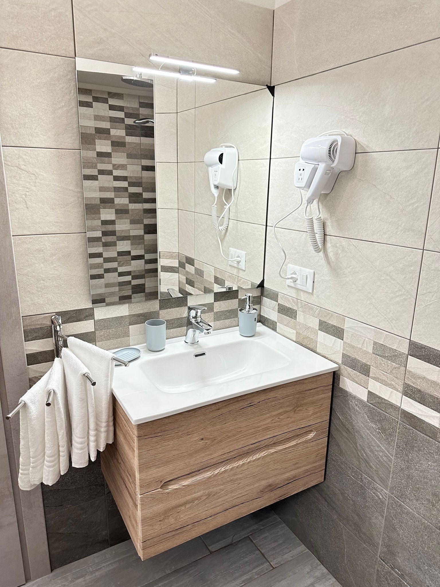 A modern bathroom with a large mirror, a sink with two faucets, and a hairdryer mounted on the wall.