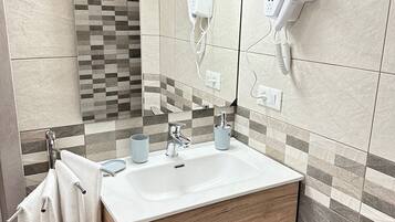 A modern bathroom with a large mirror, a sink with two faucets, and a hairdryer mounted on the wall.