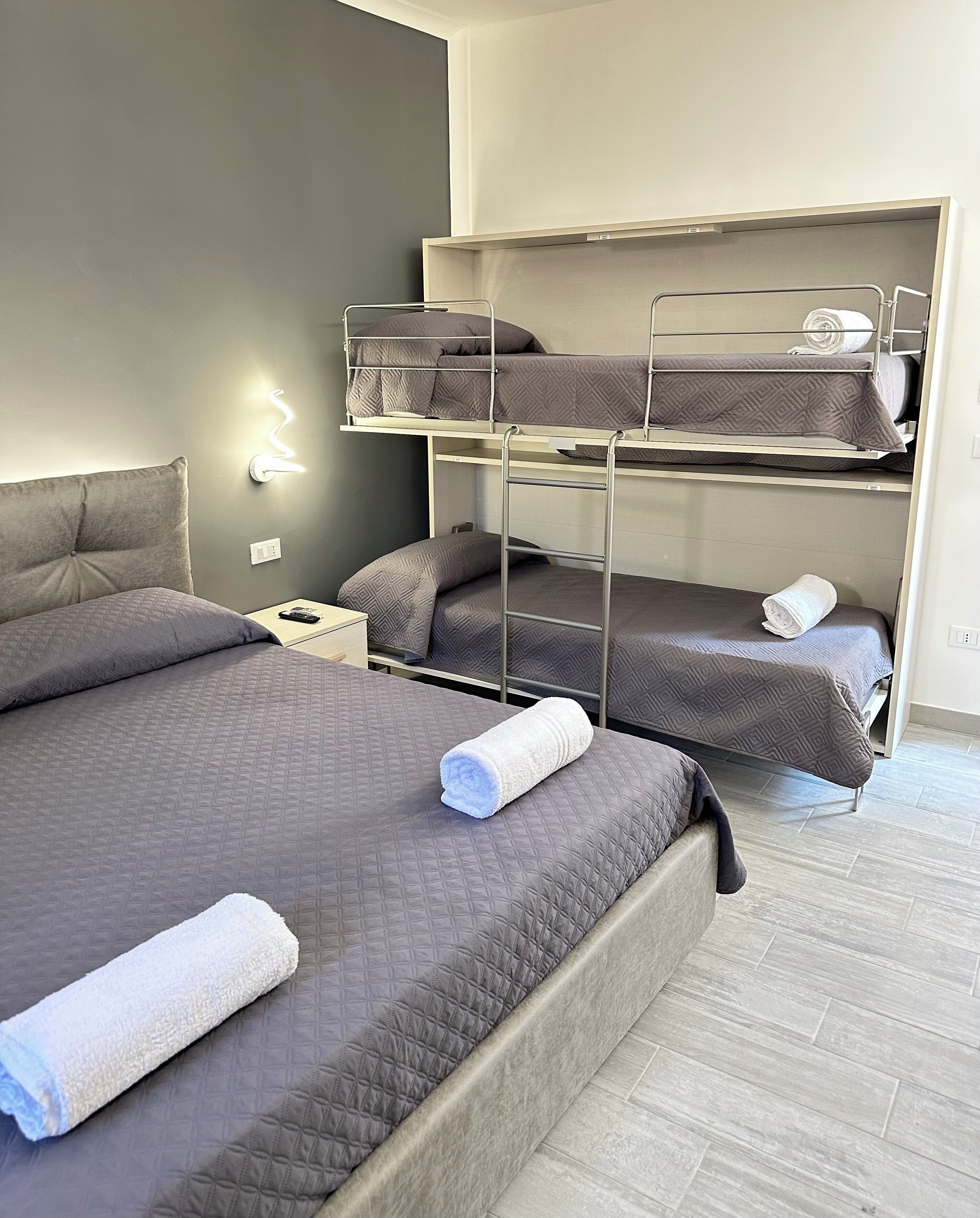 A hotel room with bunk beds, a bedside table, and a wall-mounted light.