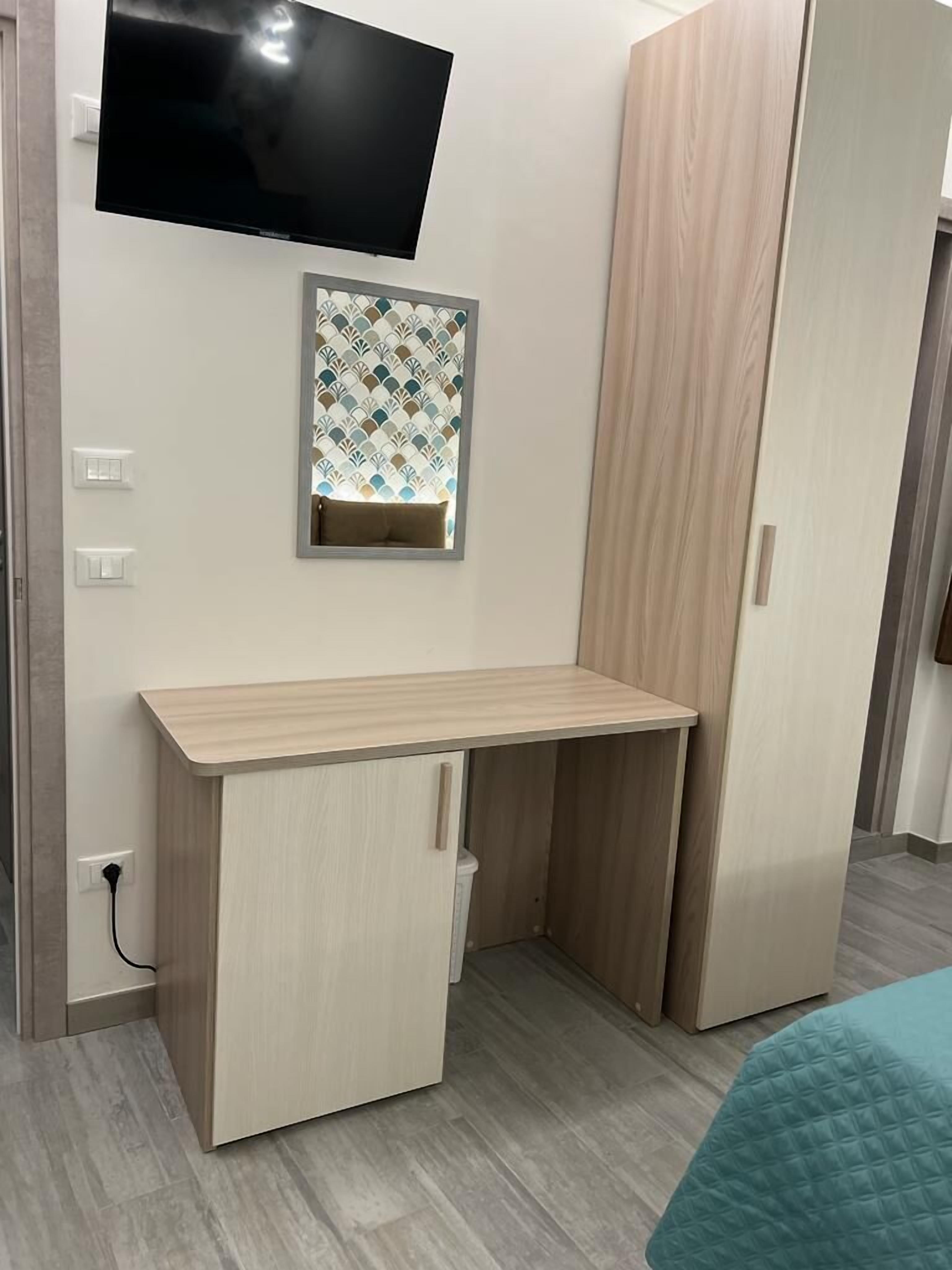 Una habitación con un escritorio de madera, un televisor montado en la pared y un espejo con motivos decorativos.