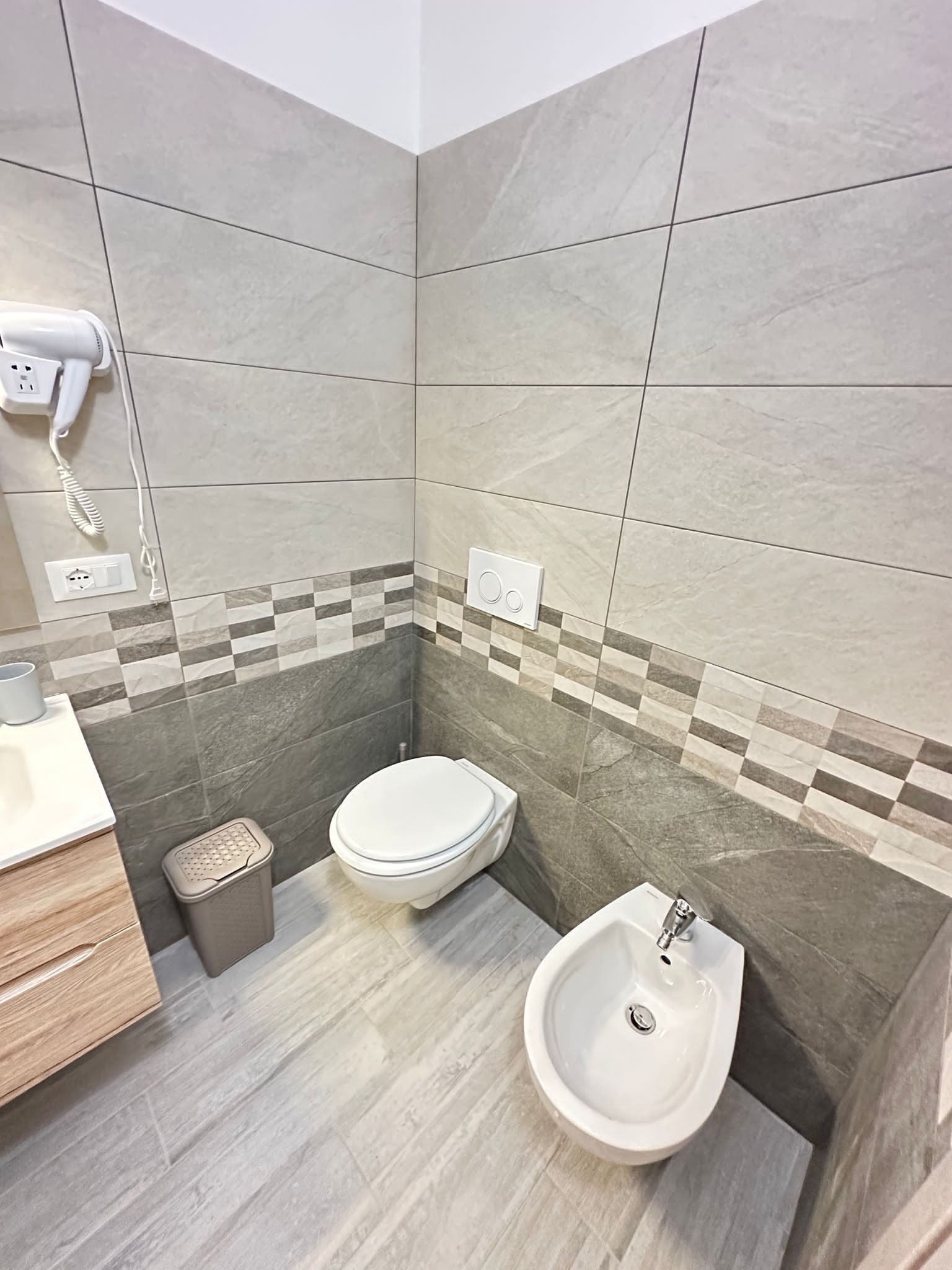 A modern bathroom with a toilet, bidet, and a hairdryer on a wall socket.
