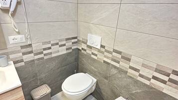 A modern bathroom with a toilet, bidet, and a hairdryer on a wall socket.
