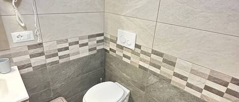 Casa de banho moderna com sanita, bidé e secador de cabelo numa tomada.