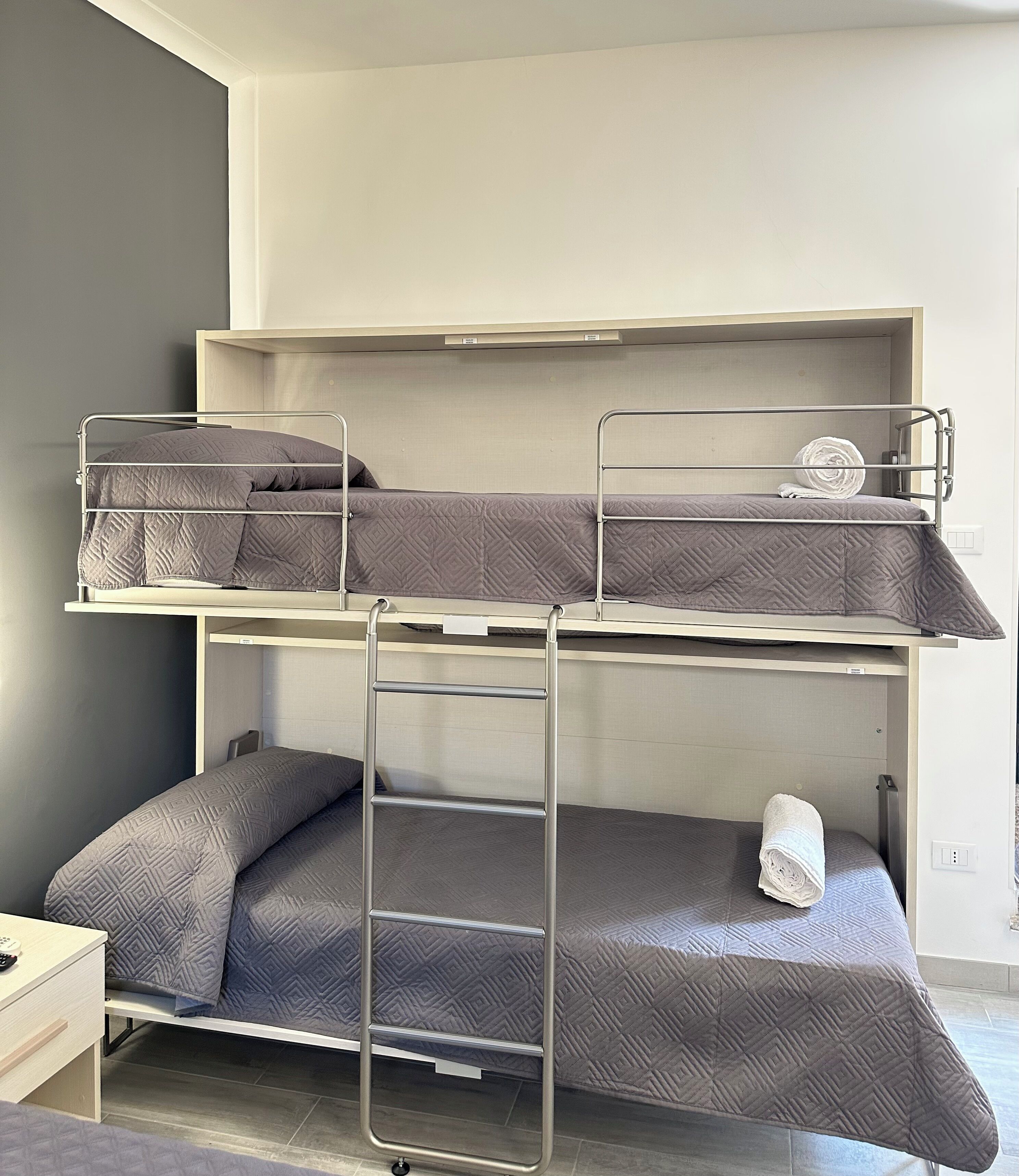 A bunk bed with a ladder, a small bedside table, and a wall-mounted light switch.