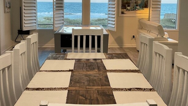 A room with a view of the ocean, a dining table with chairs, and a small table with a chair in the center.