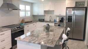 A modern kitchen with white cabinets, a stainless steel refrigerator, a granite countertop, and a built-in dishwasher.