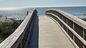 A wooden boardwalk leading to the beach with a railing on one side.