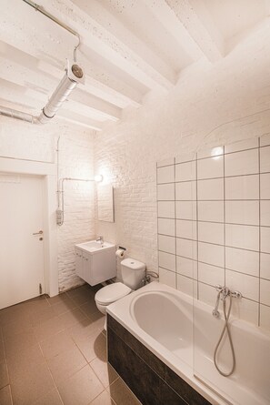 Bathroom features a bathtub, sink, and toilet, set against a backdrop of white tiles.