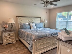 A bedroom with a bed, nightstands, lamps, a ceiling fan, and a window.