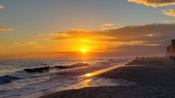 A beach with a sunset, waves, and a distant shoreline with buildings. - A 4-bedroom, 2 bath home with pond view. (Foley)