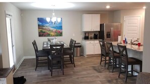 A dining area with a table and chairs, a kitchen with cabinets and appliances, and a painting on the wall. - A 4-bedroom, 2 bath home with pond view. (Foley)