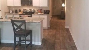 A modern kitchen with white cabinets, a central island, and a dark wooden chair. - A 4-bedroom, 2 bath home with pond view. (Foley)