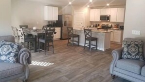 A modern kitchen with white cabinets, a central island, and a dining area with a table and chairs. - A 4-bedroom, 2 bath home with pond view. (Foley)