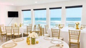 A dining area with round tables, gold chairs, and ocean views.