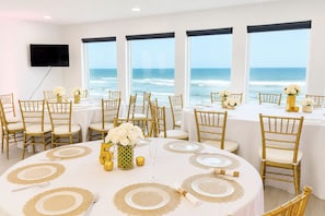 A dining area with round tables, gold chairs, and ocean views.