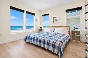 A bedroom with a bed, two bedside tables, a nightstand, a large window with a view of the beach, and a framed picture on the wall. - 6BRs with 4 Oceanfront/ featuring en suite bathrooms / Directly On The Beach (Ponte Vedra Beach)
